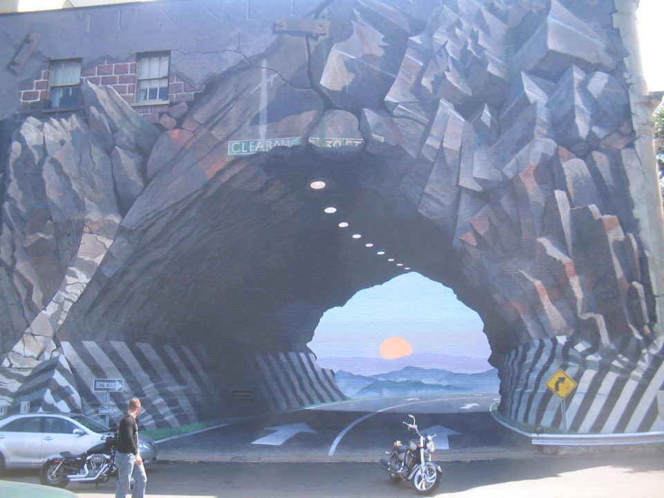 Mural depicting a tunnel with a sign reading 'CLEARANCE 10 FT' and a landscape scene visible through the opening
