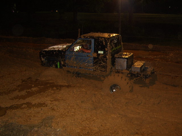 Mud-covered blue pickup truck with large tires stuck in thick mud, side view