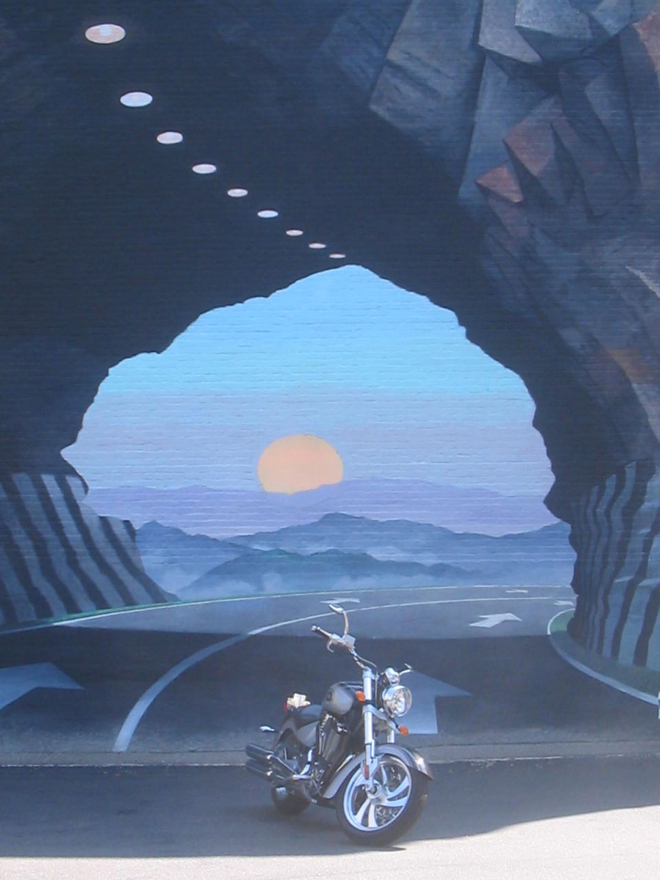 motorcycle parked in front of a tunnel opening with a sunset and mountains in the background