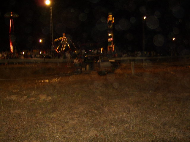 Dark truck in a muddy field at night with carnival rides in the background