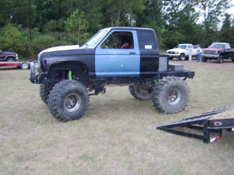 1986 Ford Ranger - A heavily modified pickup truck with large tires sits in a grassy field, with other vehicles visible in the distance.