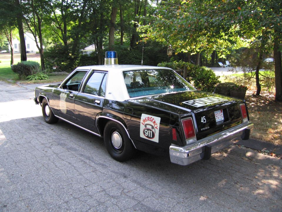 Rear view of black-and-white police sedan with Emergency 911 decal on driveway