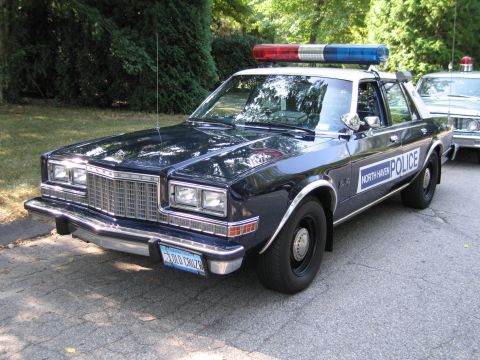 1991 Ford LTD Crown Victoria - dark blue North Haven Police sedan with a red-and-blue roof lightbar parked front-quarter on a shaded driveway.