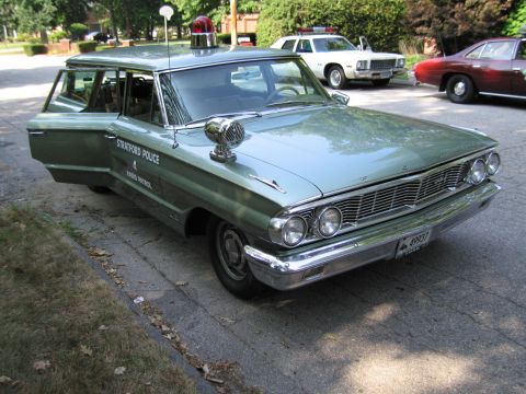 1991 Ford LTD Crown Victoria - green "Stratford Police" station wagon with chrome hood siren and roof beacon parked front-quarter on a driveway.