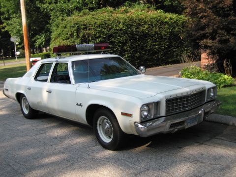 1991 Ford LTD Crown Victoria - white full-size four-door sedan fitted with a red roof lightbar is parked on a driveway in front of a green hedge.