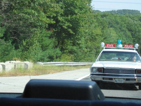1991 Ford LTD Crown Victoria - white STATE POLICE car with red roof light boxes drives along a guardrail-lined road, seen past a dashboard.