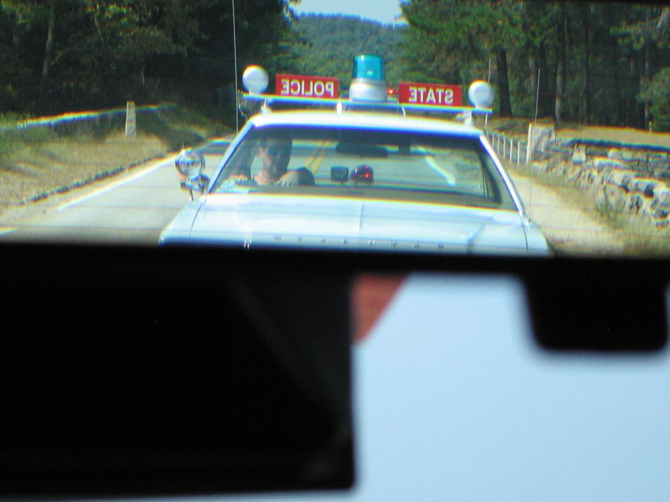 White STATE POLICE car with roof lights approaching, viewed through rear glass