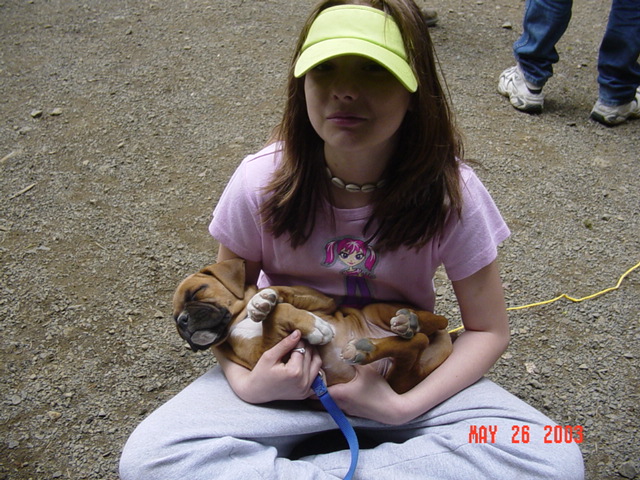 Young girl in pink shirt and yellow visor holding a small boxer puppy outdoors