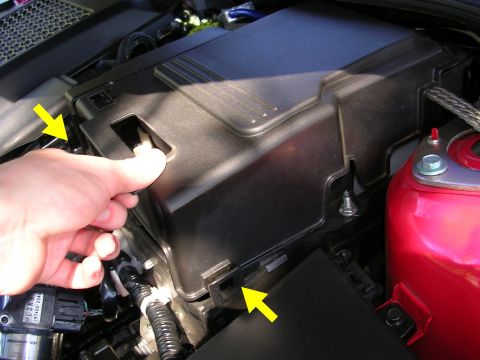 2007 Mazda 3 - Close-up of a hand interacting with a fuse box cover in a vehicle's engine bay.