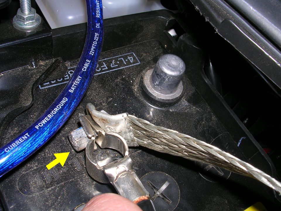Close-up of a car battery terminal with a blue power/ground cable and a braided ground strap attached