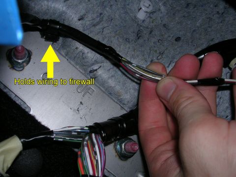 2007 Mazda 3 - Close-up of a hand manipulating a vehicle's wiring harness, secured by a clip to the firewall.