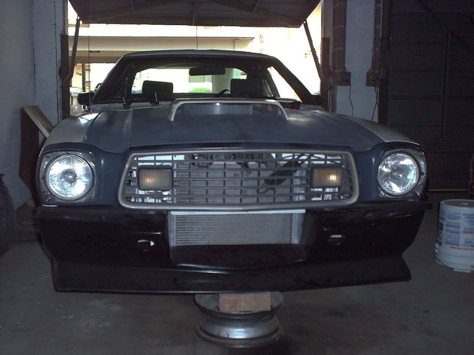 Front view of dark Mustang II hatchback in garage with hood scoop and cooler behind lower grille