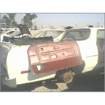 1973 Ford Ranchero - A red car door panel is placed on top of a white vehicle in a junkyard setting.