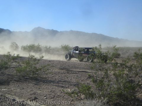 1990 Ford Bronco - small off-road buggy speeds across distant desert flats raising a long dust trail beneath hazy mountains.