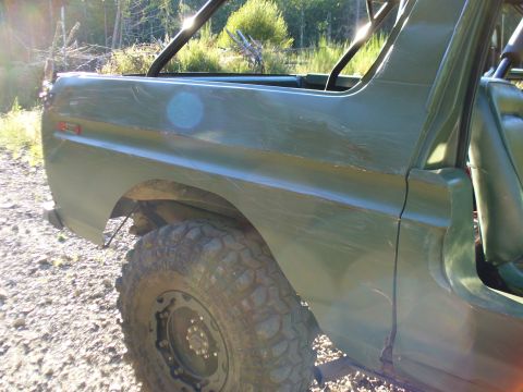 1978 Ford Bronco - The rear section of a green SUV is shown with a large off-road tire and a roll cage structure.
