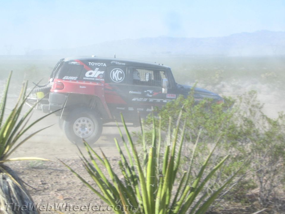 Red and black Toyota-bodied off-road race truck jumping through desert dust