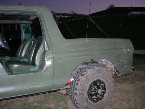 1978 Ford Bronco - Dusk shot of the passenger side of a topless flat-green Bronco parked on grass, showing the black tube roll cage, green vinyl bucket seats…