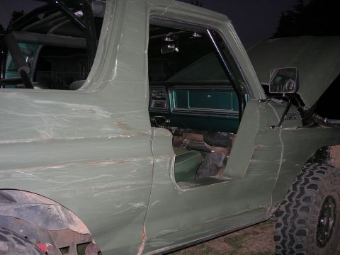 1978 Ford Bronco - Olive green 1978 Ford Bronco with open driver's door, revealing the interior and a roll cage structure.