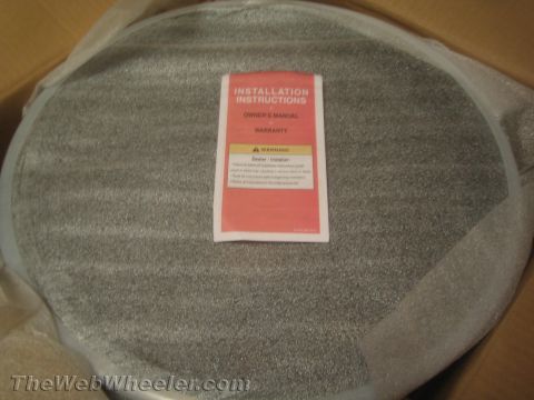 1990 Ford Bronco - Photo of an 'Installation Instructions / Owner's Manual' booklet cover lying in a box on top of a wheel.