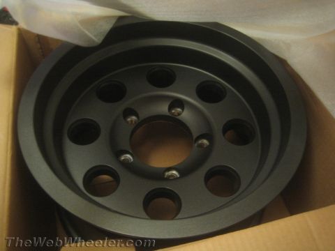 1990 Ford Bronco - black machined six-hole automotive pulley or hub with a five-lug bolt pattern sits in a cardboard box lined with packing paper.