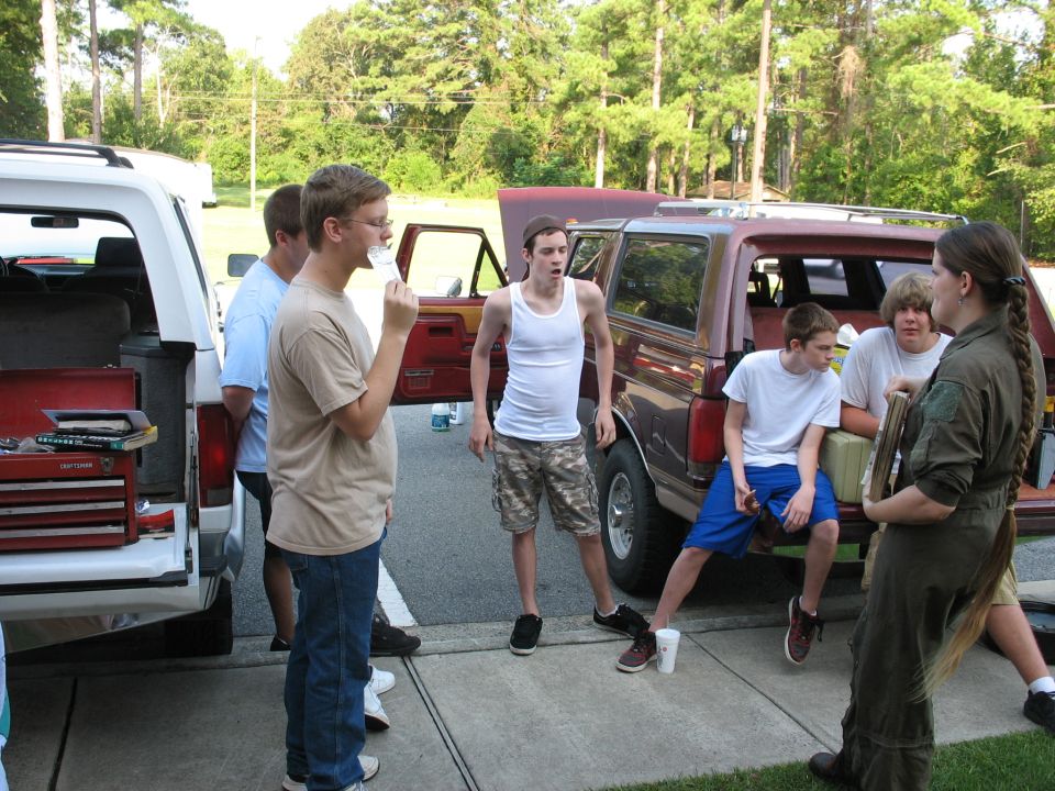 Teens gathered around a dark red four-door Ford conversion truck with doors open