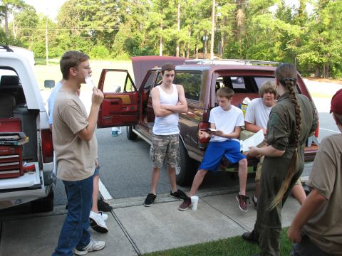 1995 Ford C-150 (Centurion Conversions) - A group of boys are gathered around a red Ford Bronco II with its hood open, possibly for a class or activity.