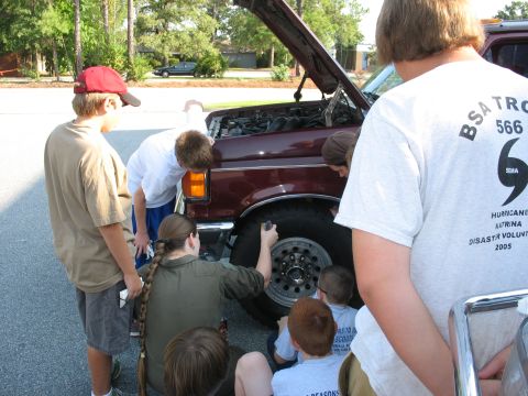1995 Ford C-150 (Centurion Conversions) - A group of people, some wearing Boy Scout attire, examine the front tire and engine of a maroon Ford truck.