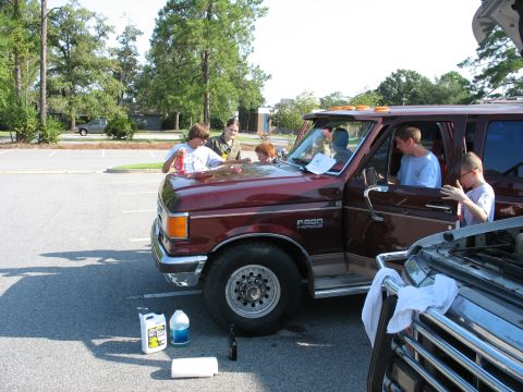 1995 Ford C-150 (Centurion Conversions) - Several people are working on a maroon 1995 Ford C-150 (Centurion Conversions) in a parking lot.