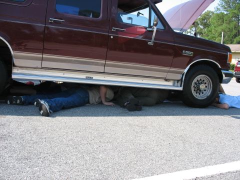 1995 Ford C-150 (Centurion Conversions) - Several individuals are working on the underside of a maroon Ford F-350, with its hood propped open.
