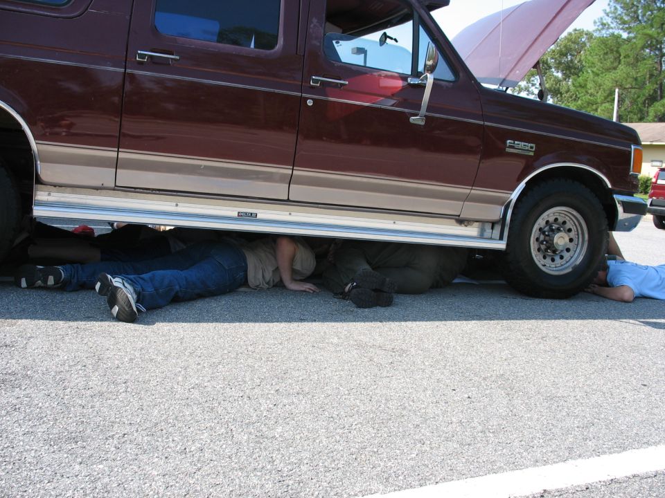 Maroon Ford F-350 with hood open, people working underneath
