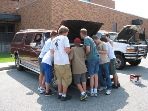 1995 Ford C-150 (Centurion Conversions) - Boys examine the engines of a maroon SUV and a white truck.