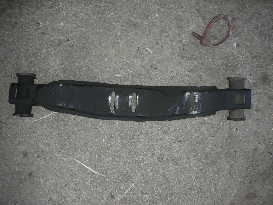 Black metal exhaust component with rubber bushings on each end, lying on a concrete surface