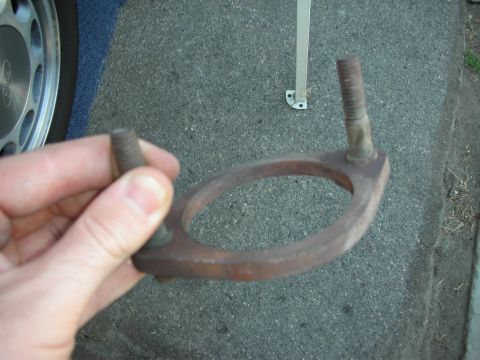 1990 Ford Mustang - A rusty exhaust flange is held up for inspection, with a car wheel and blue carpet in the background.