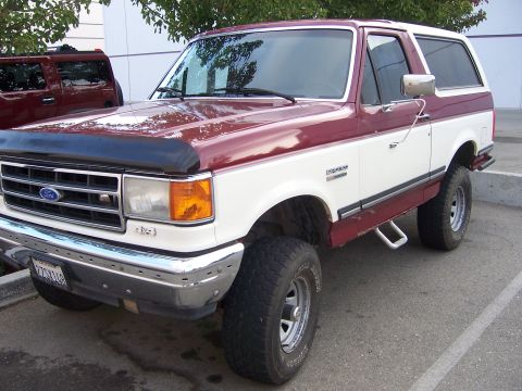 1991 Ford Bronco - This 1991 Ford Bronco features a two-tone red and white paint scheme and is shown from a 3/4 front angle.