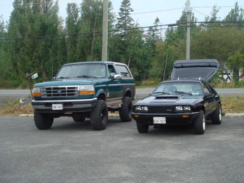 1996 Ford Bronco - Two vehicles parked outside: a green 1996 Ford Bronco and a black Ford Capri.