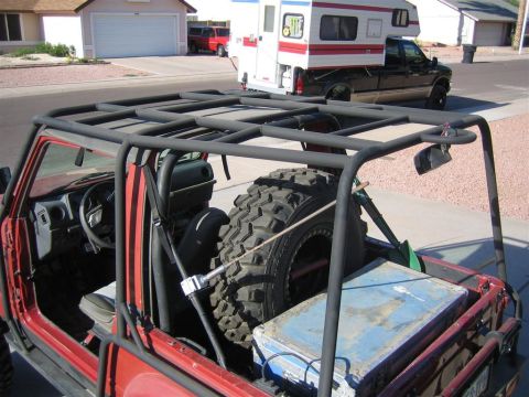 1987 Suzuki Samurai - A red 1987 Suzuki Samurai is modified with a roll cage and spare tire, parked in a driveway with other vehicles.