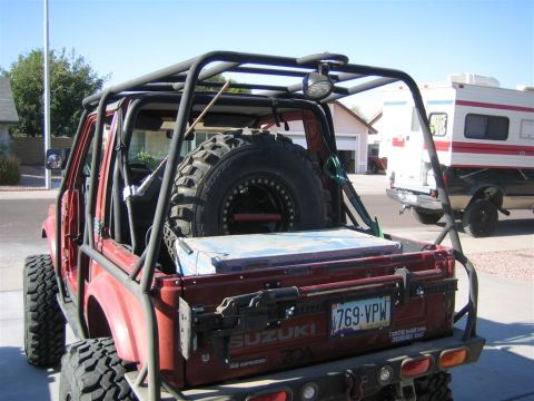 1987 Suzuki Samurai - Rear view of a red 1987 Suzuki Samurai modified with an external roll cage and a spare tire mounted on the back.