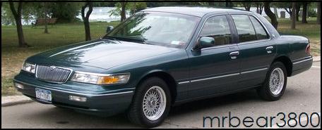 1996 Mercury Grand Marquis - A dark green sedan is parked outdoors with trees and water in the background.