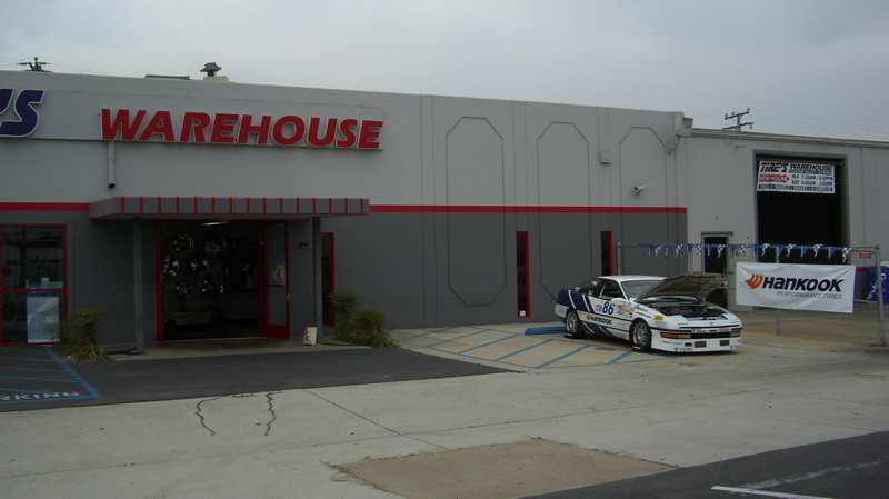 No. 86 white race coupe parked outside Tire's Warehouse beside a Hankook banner