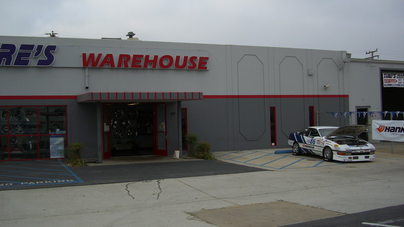 No. 86 race coupe with hood open parked outside a Tire's Warehouse shop