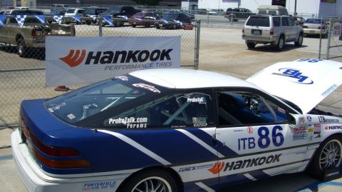 1990 Ford Probe - A race car with racing decals and a Hankook Performance Tires banner is parked at an event.