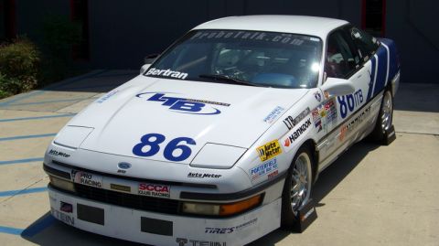 1990 Ford Probe - A white 1990 Ford Probe race car is parked outdoors, adorned with numerous sponsor decals and racing numbers.