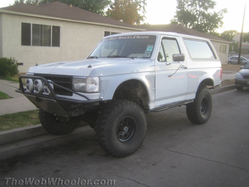 White lifted Ford Bronco with brush bar and big tires parked on a residential street