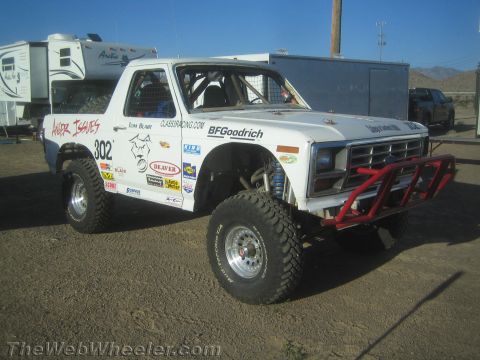 1990 Ford Bronco - white number-302 Ford prerunner race truck with a red tubular front bumper and BFGoodrich and ClassRacing.com decals sits in a desert stagi…