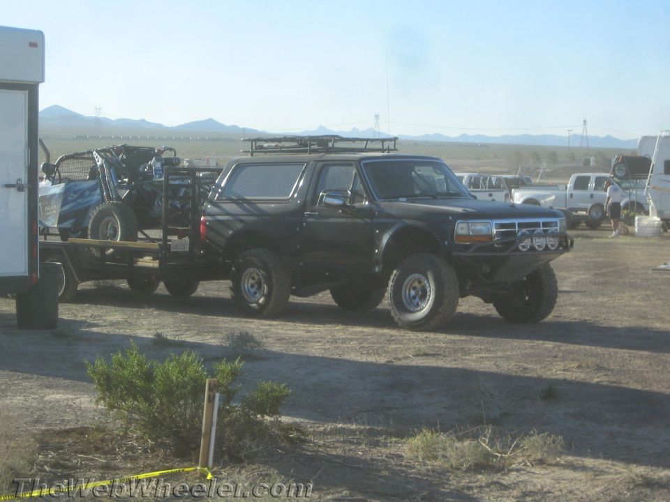 Black lifted Ford Bronco towing a trailer with a race buggy at a desert pit