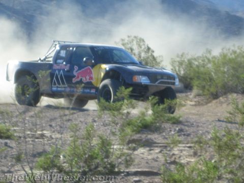 1990 Ford Bronco - black off-road prerunner race truck with Red Bull livery slides through the desert, throwing up a wall of dust amid low scrub.