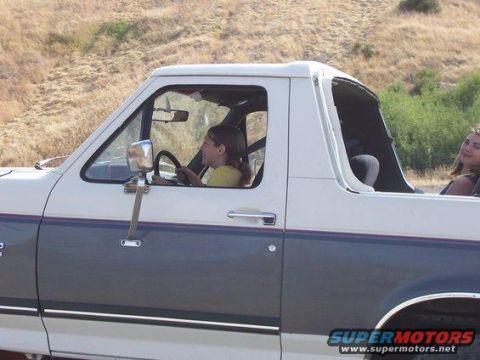 1991 Ford Bronco - Driver-side profile of a two-tone white-over-gray full-size Ford Bronco with the rear hardtop removed, showing the roll bar and open cargo…
