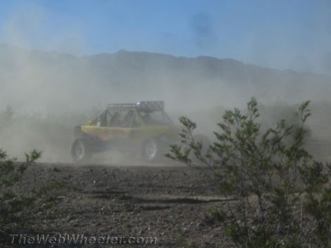 1990 Ford Bronco - yellow tube-frame off-road buggy races through thick dust on a desert course.