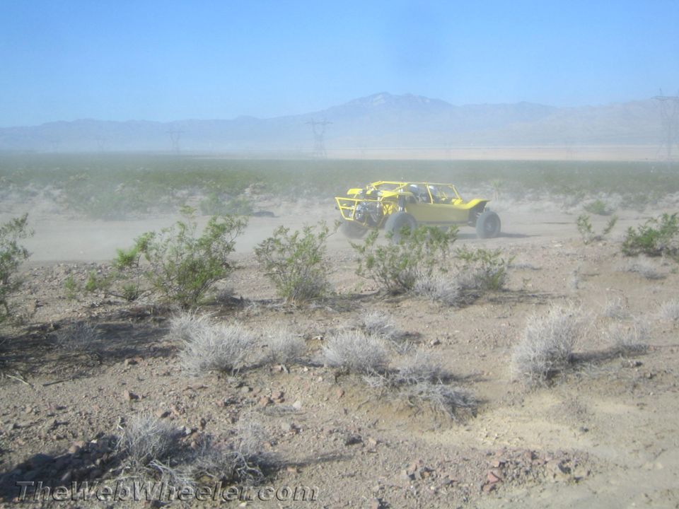 Yellow off-road buggy on a flat open desert plain with power lines and mountains