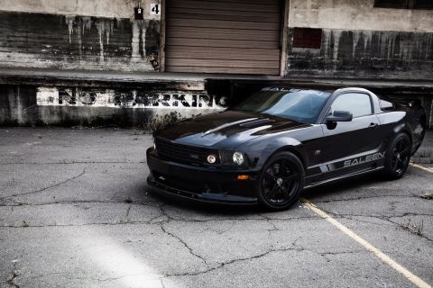 1997 Ford Probe - A black Saleen Mustang sits in front of a derelict industrial building.